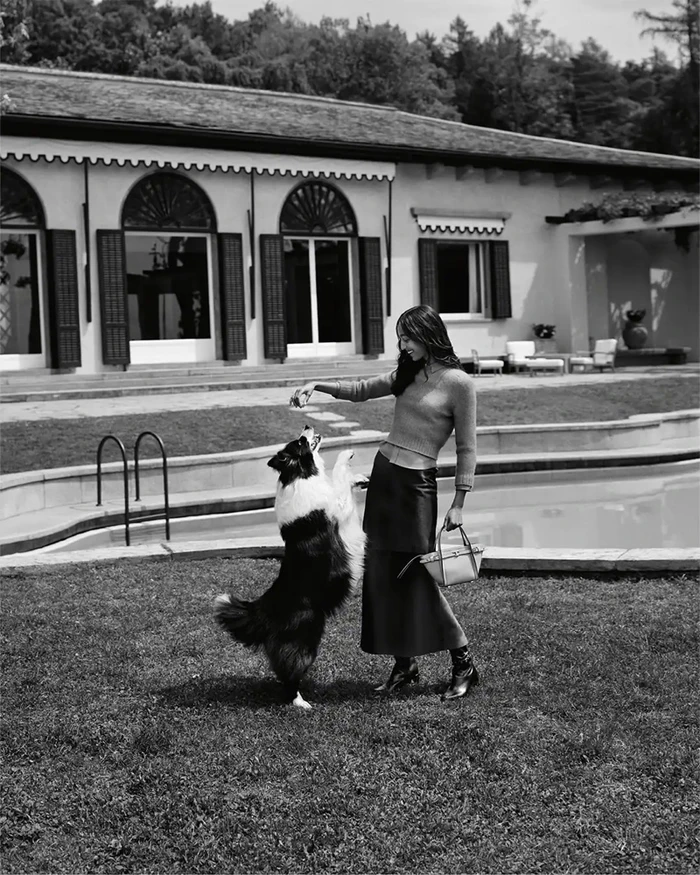 Model Mona Tougaard feeding a dog on a lawn by a pool for Tod's Italian Stories campaign