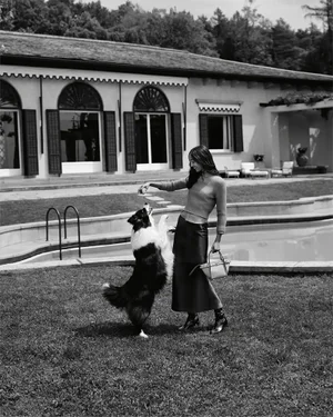 Model Mona Tougaard feeding a dog on a lawn by a pool for Tod's Italian Stories campaign