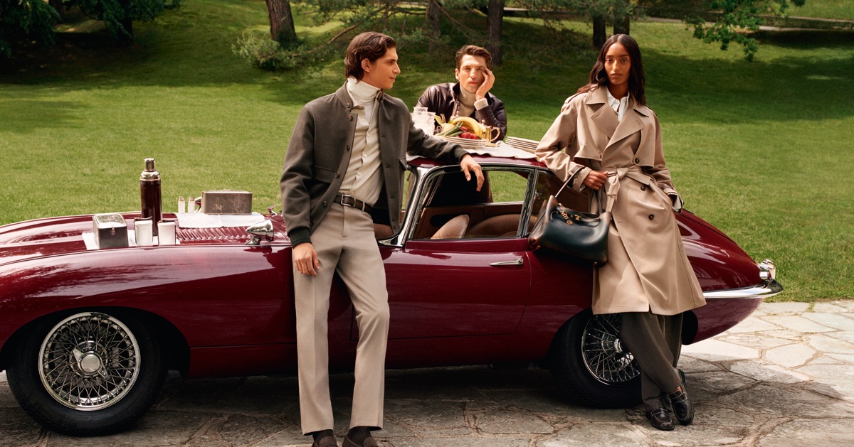 Three models posing around a vintage burgundy car outdoors on a lawn for the Tod's Italian Stories campaign