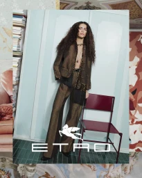 Model Adele Aldighieri posing in a metallic bronze pantsuit beside a burgundy chair for the Etro campaign.