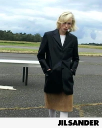 Model Edie Campbell poses in an oversized black tailored blazer and camel skirt outdoors for Jil Sander.