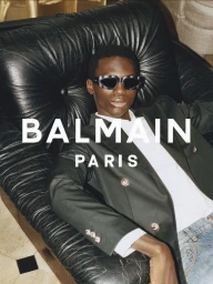 A Black man wearing sunglasses and a blazer seated on a black leather armchair for Balmain SS25.