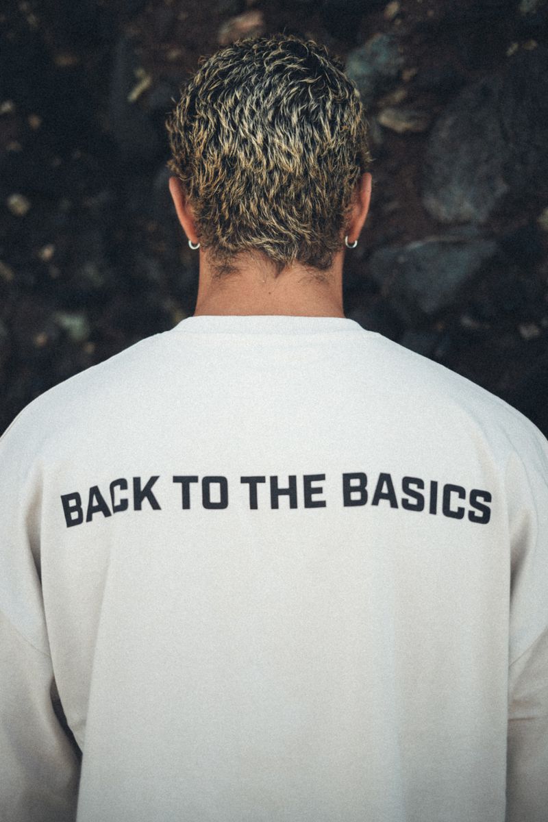 Rear view of a man with curly blonde hair wearing an off-white sweatshirt printed with BACK TO THE BASICS.