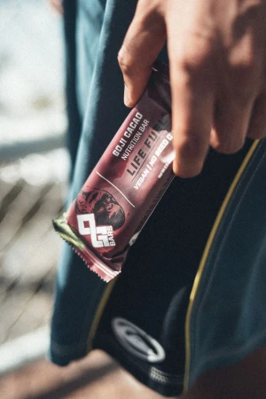 A close-up shot of a hand holding a Goji Cacao nutrition energy bar in front of dark athletic shorts.