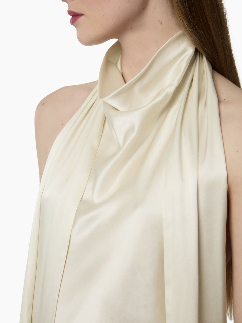 Woman wearing a cream-colored silky halter top, photographed in a studio. Fashion-forward and stylish with a focus on the fabric's texture.
