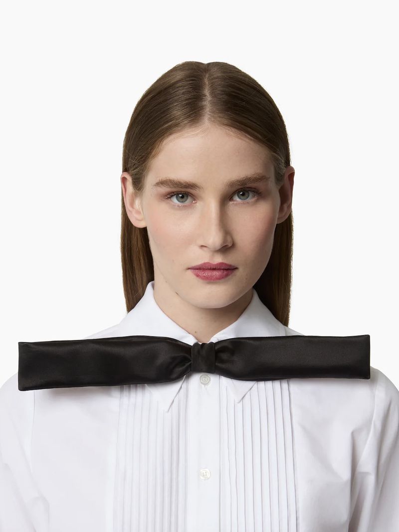 Headshot of a woman with brown hair wearing a white dress shirt and a large black bow tie against a white background.
