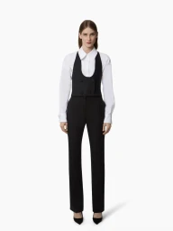 Full-length lookbook portrait of a model wearing a white collared shirt, black cropped vest, and tailored trousers on a white backdrop.