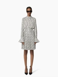 Model wearing a black and white patterned long sleeve blouse and matching pleated skirt against a white studio background.