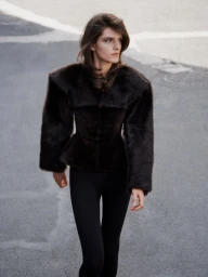 Model walking on an asphalt street wearing a dark brown fur jacket with wide lapels and black trousers.