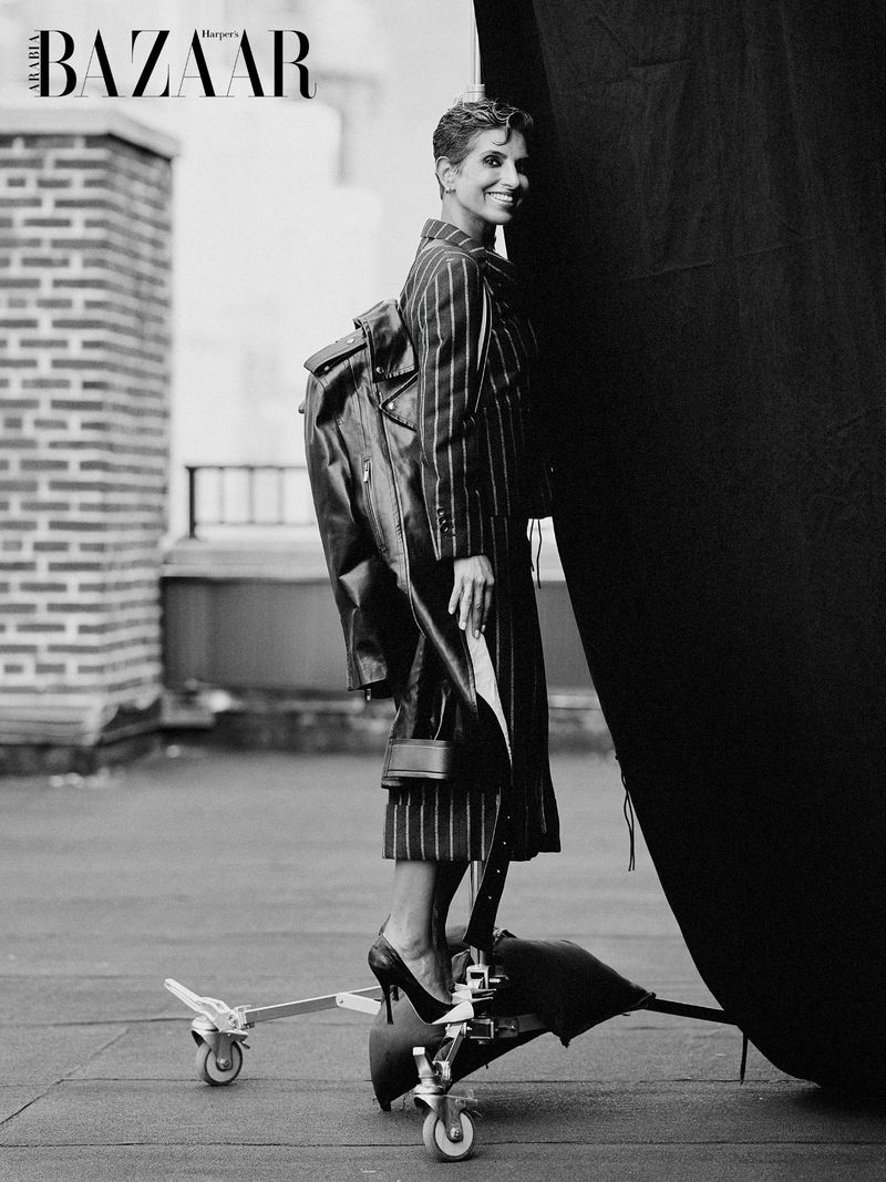 Deena Aljuhani Abdulaziz wearing a pinstripe suit and high heels while balancing on a studio backdrop stand on a rooftop.