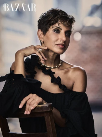 Princess Deena Aljuhani Abdulaziz wearing a black off-shoulder ruffled dress and gold choker, leaning on a wooden chair.