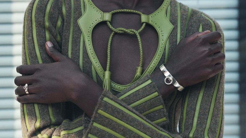 Close-up of a stylish adult wearing a brown and green striped sweater with ornamental neckline, silver ring and bracelet.