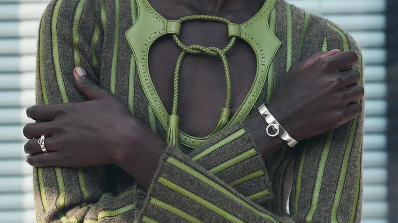 Close-up of a stylish adult wearing a brown and green striped sweater with ornamental neckline, silver ring and bracelet.