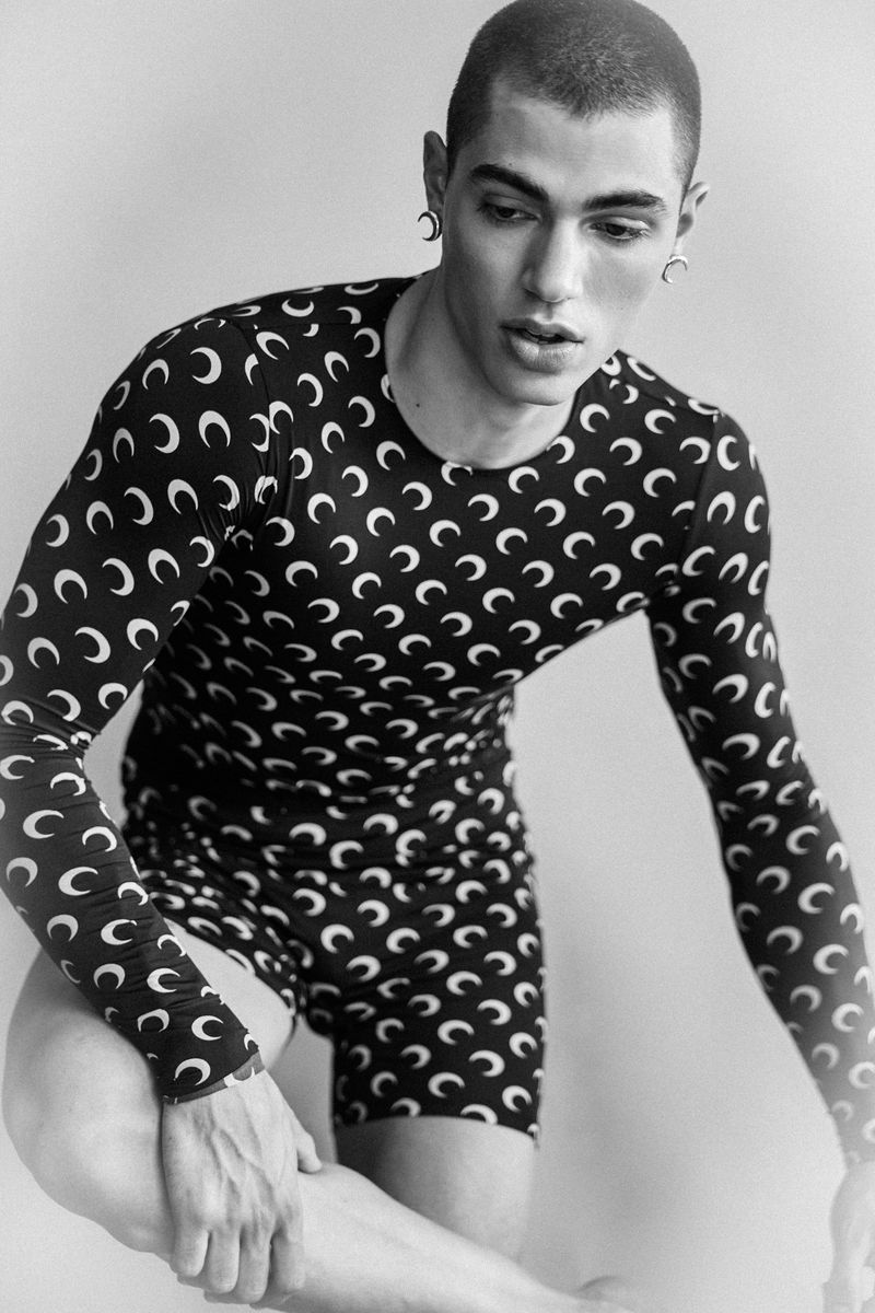 Model Ruben Aires poses in a crescent moon pattern long-sleeve bodysuit against a plain studio background.