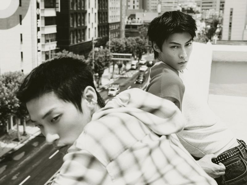 Two men looking from a rooftop ledge over an urban street in a black and white fashion editorial shoot.