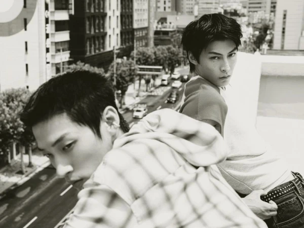 Two men looking from a rooftop ledge over an urban street in a black and white fashion editorial shoot.