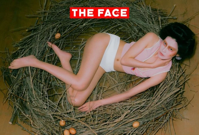 An East Asian model lying in a large twig nest with brown eggs, wearing a pink sleeveless top and white briefs.