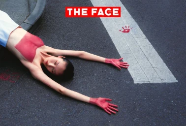 Model with red painted hands and chest lying on an asphalt road next to a white painted road marking and a red handprint.