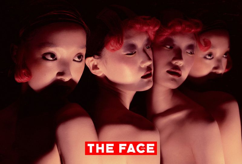 Dramatic editorial portrait of East Asian models with red curled bangs and bare shoulders in warm chiaroscuro lighting.