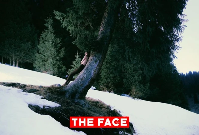 Model leaning back against a large pine tree trunk on a snow-covered hillside in a pine forest for The Face China.