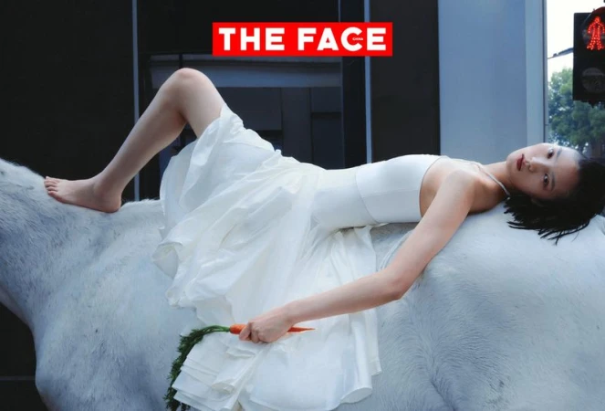 Model in a white dress lying on her back across a white horse on a city street while holding a carrot.