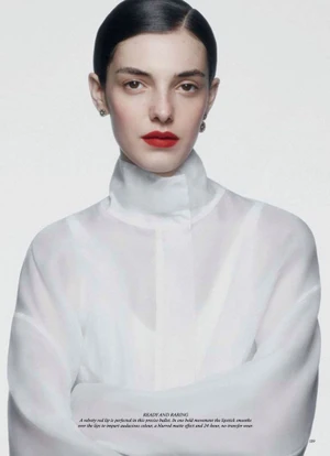 Model Carla Rey with sleek dark hair and bold red lips wearing a sheer high-neck white blouse against a white studio backdrop.