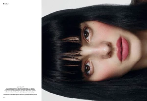 Close-up beauty portrait of a model with straight black hair and blunt bangs wearing pink lipstick for a magazine editorial spread.