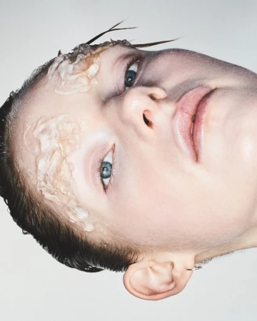 Close-up portrait of a model with textured translucent gel applied near the eye and temple against a pale background.