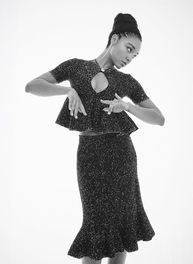Monochrome studio portrait of a woman in a sparkling textured peplum top and matching midi skirt posing against a white backdrop.