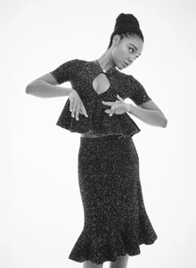 Monochrome studio portrait of a woman in a sparkling textured peplum top and matching midi skirt posing against a white backdrop.
