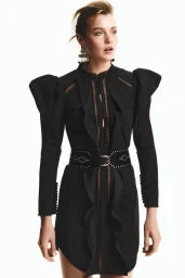 Model wearing a black ruffled dress with statement shoulders and a studded belt against a white background