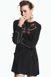 Ella McCutcheon wearing a black embroidered long-sleeve mini dress against a white studio background for Isabel Marant.