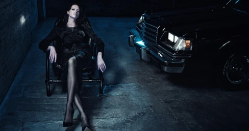 Model Irina Shayk seated in a black chair next to a vintage car in a dark garage for Agent Provocateur Neo-Diva