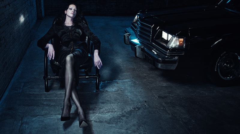 Model Irina Shayk seated in a black chair next to a vintage car in a dark garage for Agent Provocateur Neo-Diva