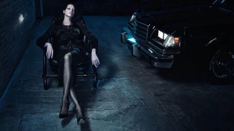 Model Irina Shayk seated in a black chair next to a vintage car in a dark garage for Agent Provocateur Neo-Diva