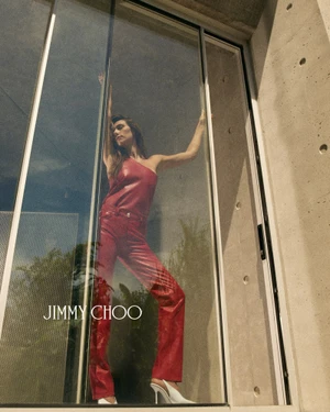 Devon Lee Carlson posing in a red leather outfit behind glass for Jimmy Choo Wardrobe Collection 2026