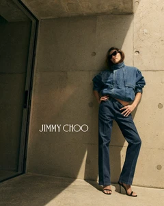 Devon Lee Carlson wearing denim jacket and trousers leaning against a concrete wall for Jimmy Choo