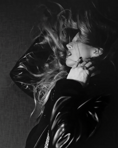 Raquel Zimmermann with windblown hair wearing a dark leather jacket in a black and white portrait for Khaite.