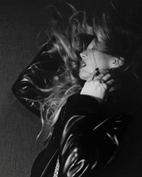 Raquel Zimmermann with windblown hair wearing a dark leather jacket in a black and white portrait for Khaite.