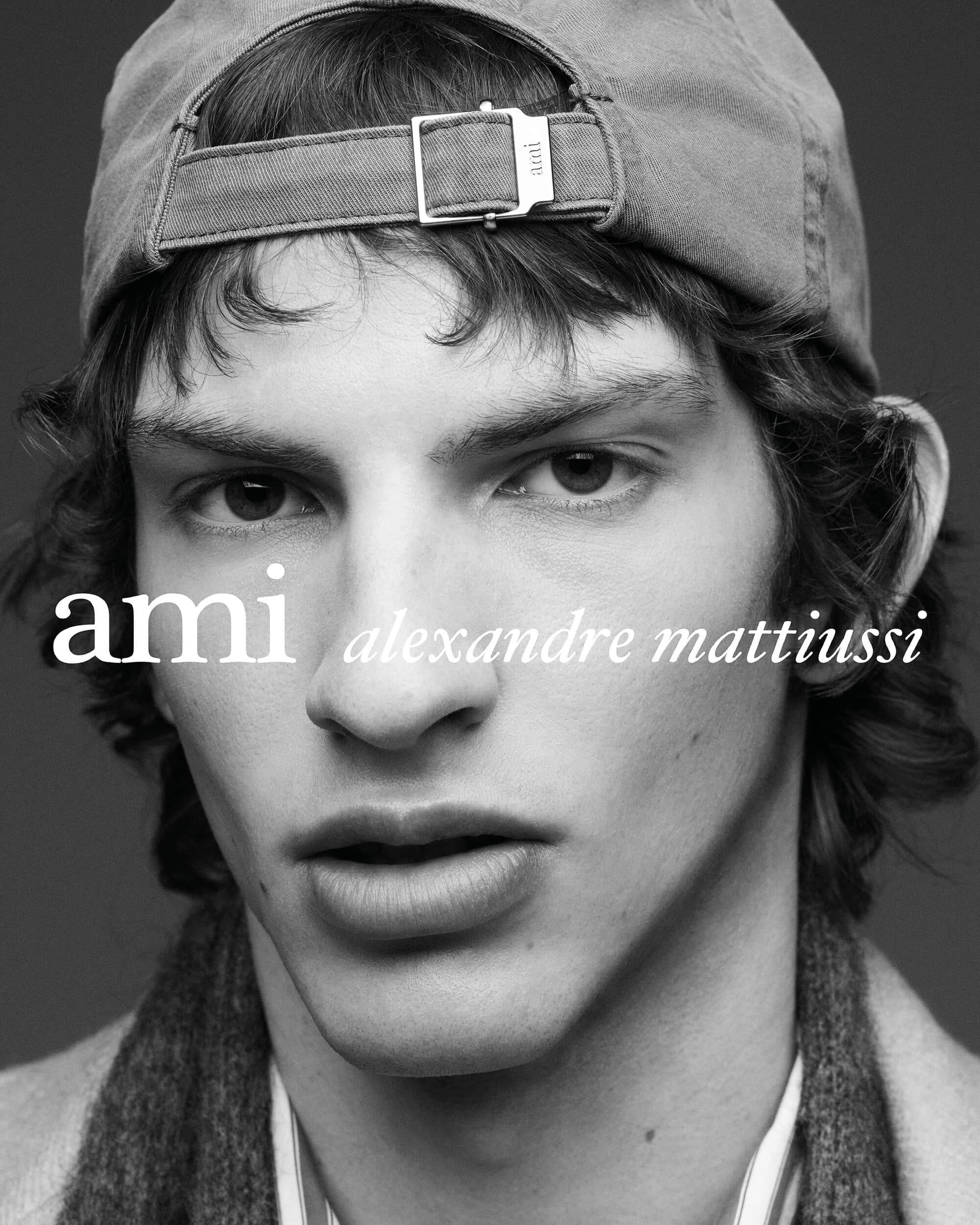 Black and white close-up portrait of a young man wearing a backward cap with the Ami Alexandre Mattiussi logo overlaid.