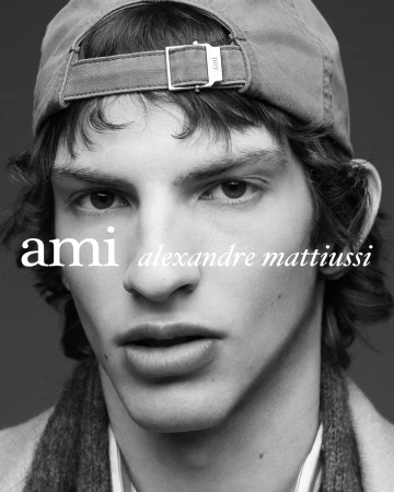 Black and white close-up portrait of a young man wearing a backward cap with the Ami Alexandre Mattiussi logo overlaid.