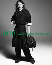 Jingwen Jia wearing a black jacket and pleated skirt holding a black backpack in Ami Paris Fall 2026 campaign.