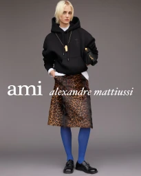 Model wearing a black hoodie, leopard-print skirt, and bright blue tights against a neutral grey studio backdrop for Ami Paris.