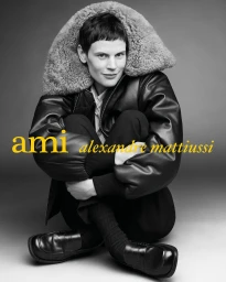 Model Saskia de Brauw seated hugging her knees in an oversized black leather shearling jacket and loafers for Ami Paris.
