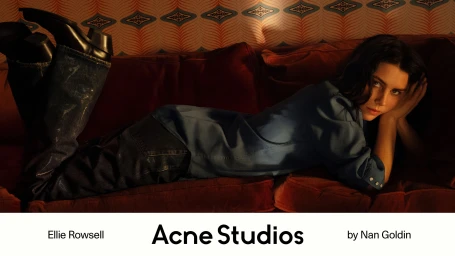 Ellie Rowsell lying on a red velvet couch wearing a blue denim shirt, dark jeans, and black boots for Acne Studios.