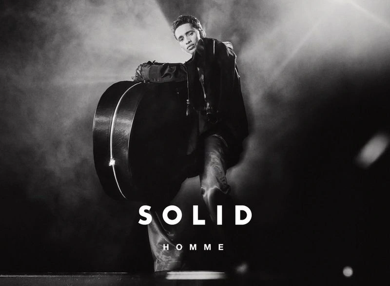 Model Abdallah El Farjani poses with a large rounded hard case under dramatic spotlight for the Solid Homme F/W 2025 campaign.