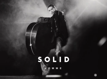 Model Abdallah El Farjani poses with a large rounded hard case under dramatic spotlight for the Solid Homme F/W 2025 campaign.