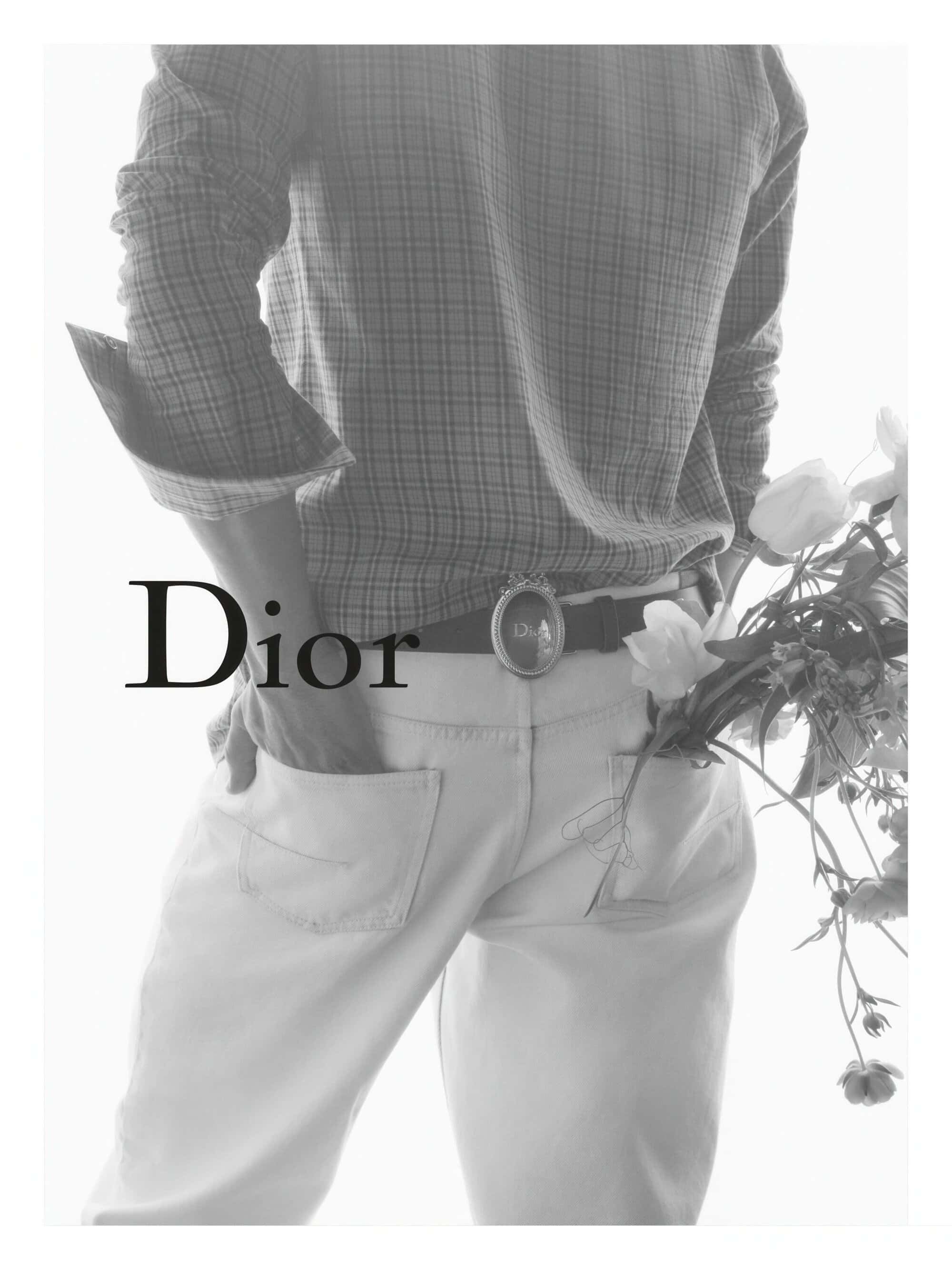 Monochrome shot of a model from the chest down in a plaid shirt and white trousers holding flowers for Dior Winter 2026.