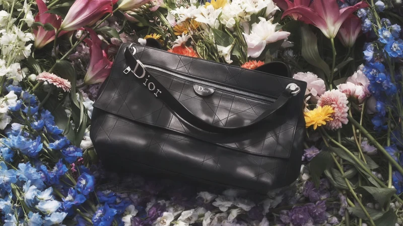Black leather Dior handbag with Cannage geometric stitching resting atop an arrangement of vibrant colorful flowers.