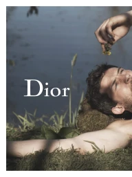 Josh O'Connor lying shirtless on grass beside water with a hand dangling a flower above him for Dior.